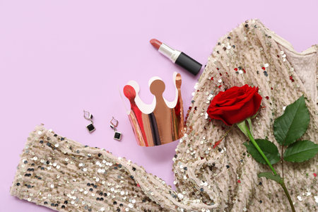 Paper crown with stylish dress, lipstick, earrings and beautiful rose on lilac background. Prom conceptの写真素材