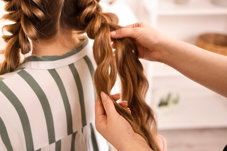 Professional hairdresser braiding client's hair in salon, closeup