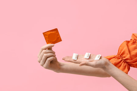Female hands with vaginal suppositories and condom on pink backgroundの写真素材