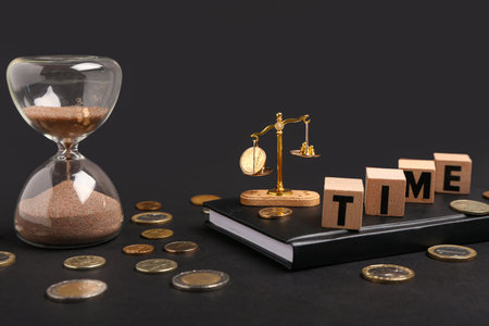 Cubes with the word TIME, mini scales with coins and hourglass on black background. Time management...