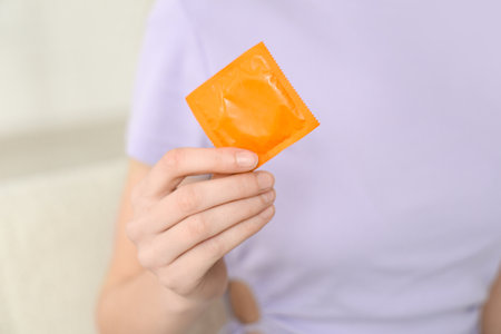 Young woman with condom on light background, closeupの写真素材
