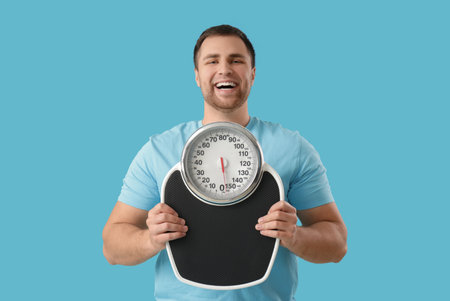 Young man with weight scales on blue backgroundの写真素材