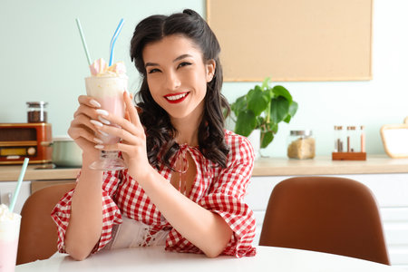 Beautiful pin-up waitress with glass of cocktail sitting at table in cafeの写真素材