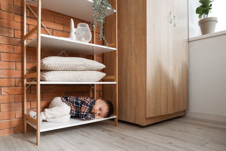 Little boy lying on shelf at home. Child in dangerの写真素材