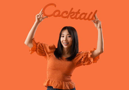Young Asian woman holding word shaped sign with text COCKTAIL on orange background