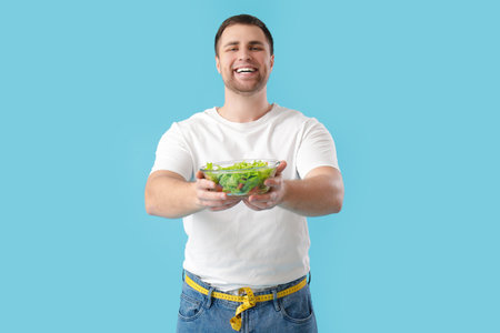 Young man with salad on blue background. Weight loss conceptの写真素材