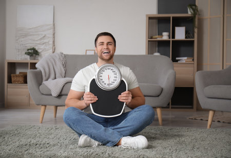 Young man with scales sitting at home. Weight loss conceptの写真素材