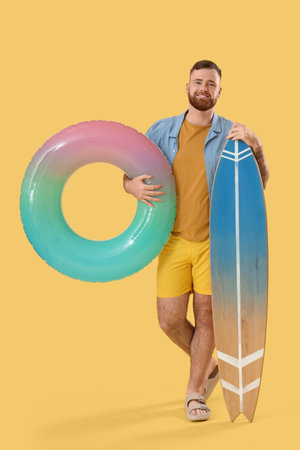 Young man with inflatable ring and surfboard on yellow backgroundの写真素材