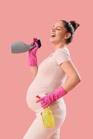 Young pregnant woman with spray bottles of detergent on pink backgroundの写真素材