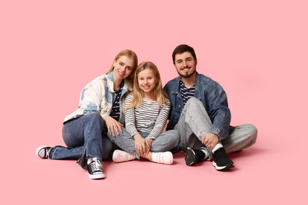 Happy family in stylish denim clothes sitting on pink backgroundの写真素材