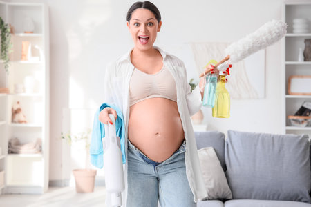 Surprised young pregnant woman different cleaning supplies at homeの写真素材