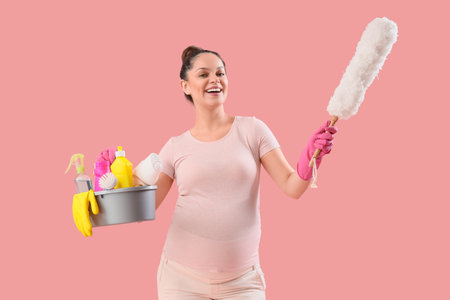 Young pregnant woman with pp-duster and cleaning supplies on pink backgroundの写真素材