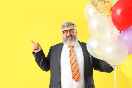 Senior businessman with bunch of colorful balloons on yellow backgroundの写真素材
