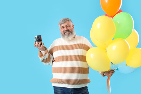Senior man with bunch of balloons and photo camera on blue backgroundの写真素材
