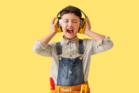 Cute little builder in hearing protectors shouting on yellow backgroundの写真素材