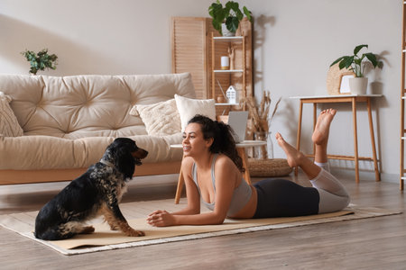 Sporty young African-American woman with cocker spaniel lying on yoga mat at homeの写真素材