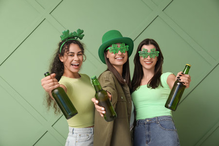 Beautiful young women with bottles of beer on green background. St. Patrick's Day celebration