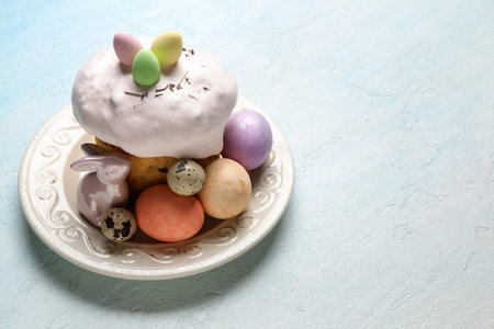 Plate with Easter cake and painted eggs on light blue background
