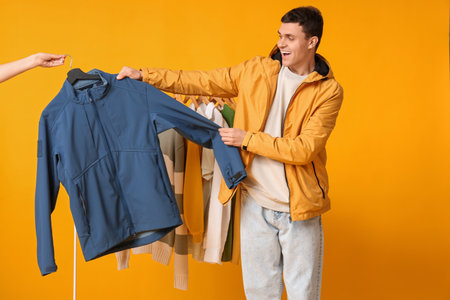 Handsome young happy man and rack with stylish clothes on yellow backgroundの写真素材