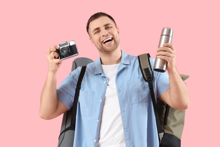 Male tourist with backpack, flask and photo camera on pink backgroundの写真素材