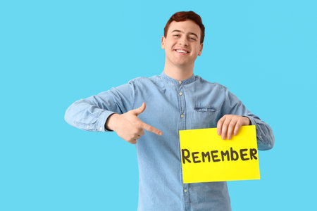 Young man pointing at paper with the word REMEMBER on blue backgroundの写真素材
