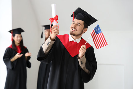 Male graduate student with diploma and USA flag in light roomの写真素材