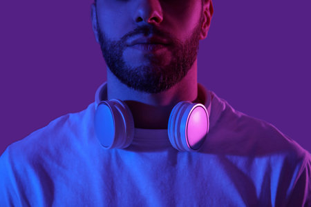Young man in modern headphones on purple background, closeup