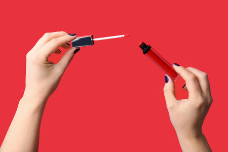 Female hands with liquid lipstick on red background
