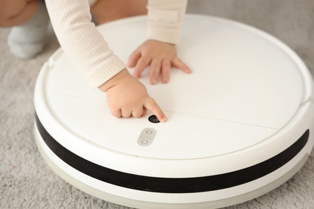 Cute little baby with robot vacuum cleaner at home, closeupの写真素材