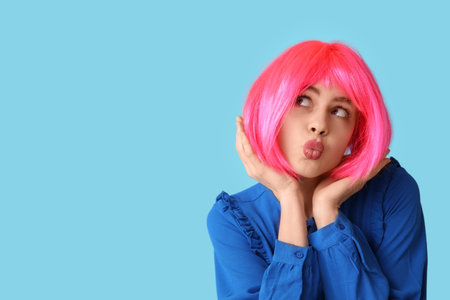 Beautiful young woman in funny disguise blowing kiss on blue background. April Fools Day celebrationの写真素材