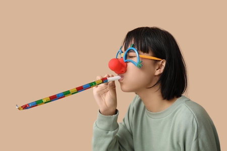 Beautiful young woman in funny disguise with party whistle on brown background. April Fools Day celebrationの写真素材
