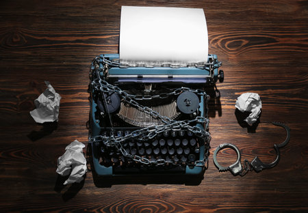Vintage typewriter with chains, handcuffs and crumpled paper on wooden background. Printing ban conceptの写真素材