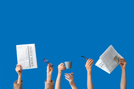 Female hands holding newspapers with eyeglasses, cup of coffee and smoking pipe on blue backgroundの写真素材