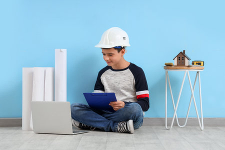 Little architect with clipboard and laptop near blue wallの写真素材