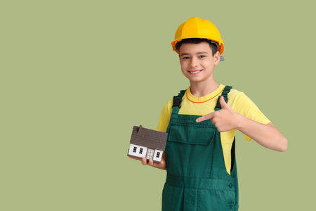 Little architect in hardhat pointing at house model on green backgroundの写真素材