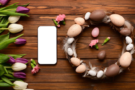 Composition with modern mobile phone, beautiful flowers and Easter wreath on wooden backgroundの写真素材