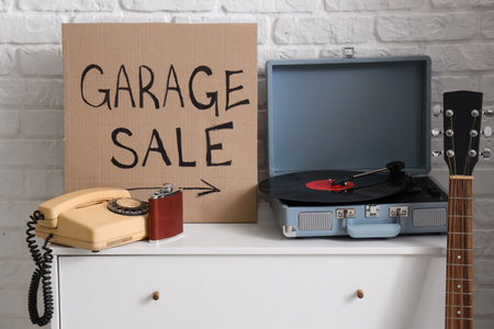 Many various unwanted things and cardboard with text GARAGE SALE near white brick wall in roomの写真素材