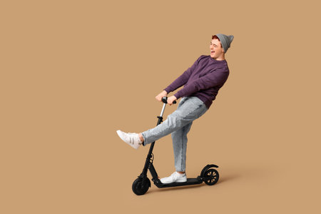 Young man riding modern electric kick scooter on brown backgroundの写真素材