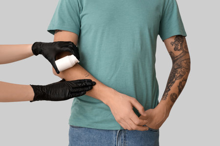 Tattoo master applying cream on man's arm against light background, closeupの写真素材