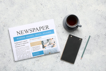 Newspaper with notebook, pencil and cup of tea on gray grunge backgroundの写真素材
