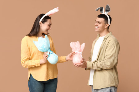 Happy young couple with Easter bunny ears and gifts on beige background