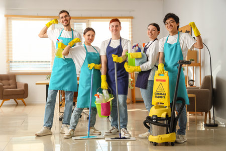 Group of young janitors with cleaning supplies in officeの写真素材