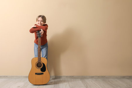 Cute little boy with guitar on beige backgroundの写真素材