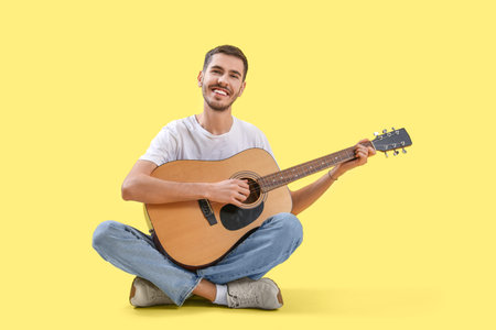 Handsome young man playing guitar on yellow background