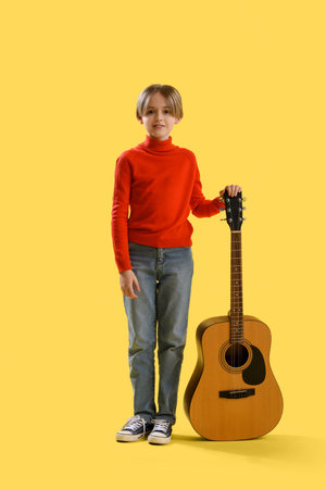 Cute little boy with guitar on yellow backgroundの写真素材