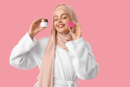 Beautiful Muslim woman in hijab with heart-shaped sponge and cream on pink backgroundの写真素材