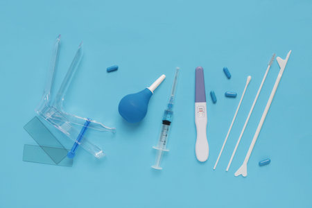 Gynecological speculum with pap smear test tools, pregnancy test and enema on blue background