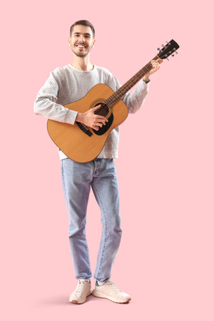 Handsome young man playing guitar on pink backgroundの写真素材