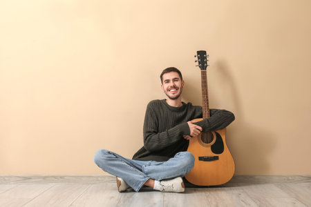 Handsome young man with guitar on beige backgroundの写真素材