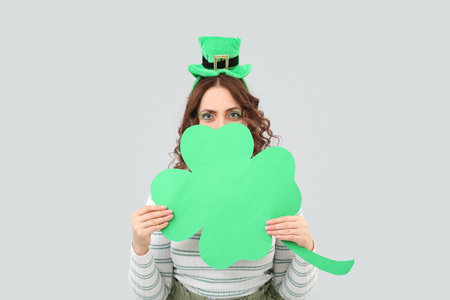 Happy woman with paper clover celebrating St. Patrick's Day on light background